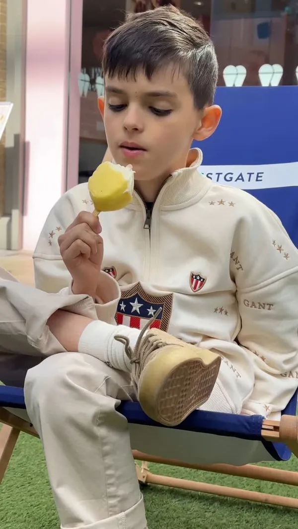 The video promotes Snowflake Gelato, focusing on their unique lemon-shaped gelato popsicles. It features close-ups of the popsicles in a display case, shows them served on plates, includes a shot of the shop interior highlighting their use of organic milk, and shows a hand holding a popsicle and a child eating one.