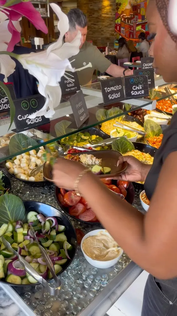 The video documents a visit to Preto Brazilian BBQ restaurant in Putney, London. It showcases the unlimited meat service (Rodizio grill) with various cuts of beef and chicken being carved tableside. The extensive buffet/salad bar is also featured, displaying a wide selection of sides including pasta salad, rice, vegetables, bread, and plantain chips. The influencer is shown selecting food from the buffet, eating, and expressing positive reactions. The video concludes with shots of desserts and the influencer posing.