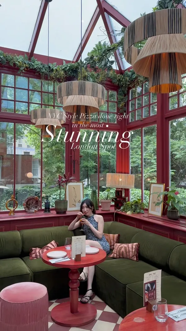 The video showcases a visit to EVE Kensington, a restaurant in London. It features shots of the restaurant's interior, including a conservatory area with lush greenery and stylish decor, as well as an outdoor seating area. The video highlights several dishes: a Romana pizza topped with burrata and cured pork, a Hawaiian pizza with pineapple and pickled jalapeños, a Caesar salad, and buffalo fried chicken wings. The video shows a person enjoying the food and the ambiance.