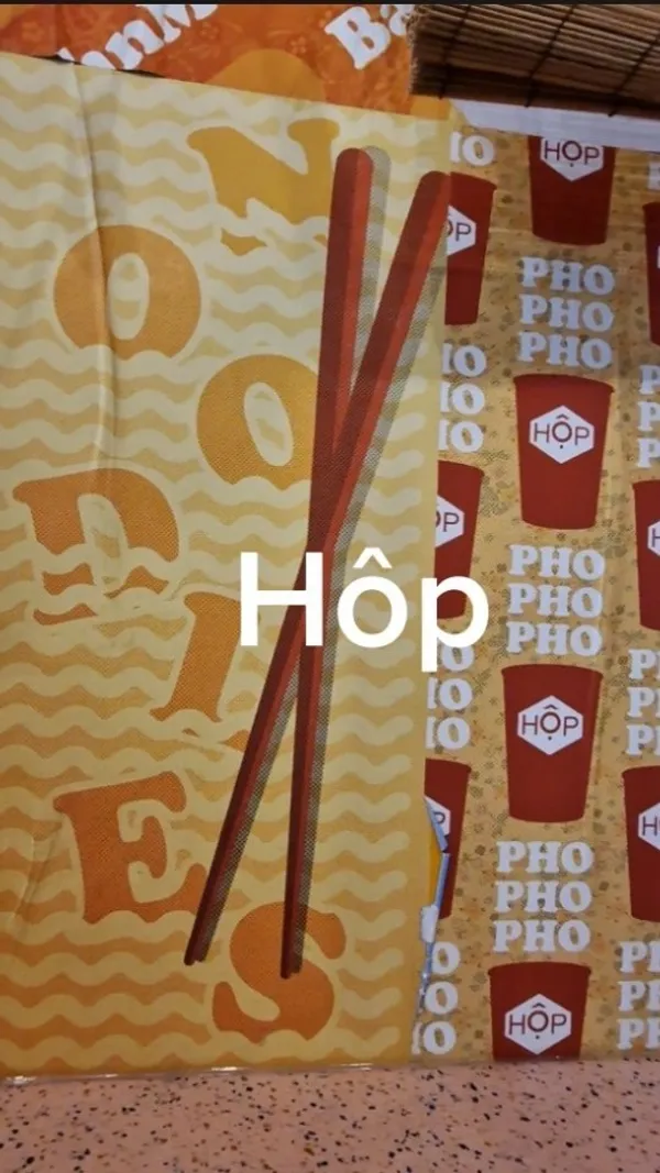 The video showcases Hop Vietnamese, a fast-casual Vietnamese restaurant in London. It highlights their menu, which includes pho (beef brisket, chicken, pulled mushrooms, prawn dumplings, chargrilled pork), rice boxes, noodle salads, and banh mi baguettes. The video shows a customer ordering on a digital kiosk, and then shows several shots of the food, including a close-up of a pho and a woman eating a curry-like dish. The video also briefly shows the interior of the restaurant and the order pick-up area.