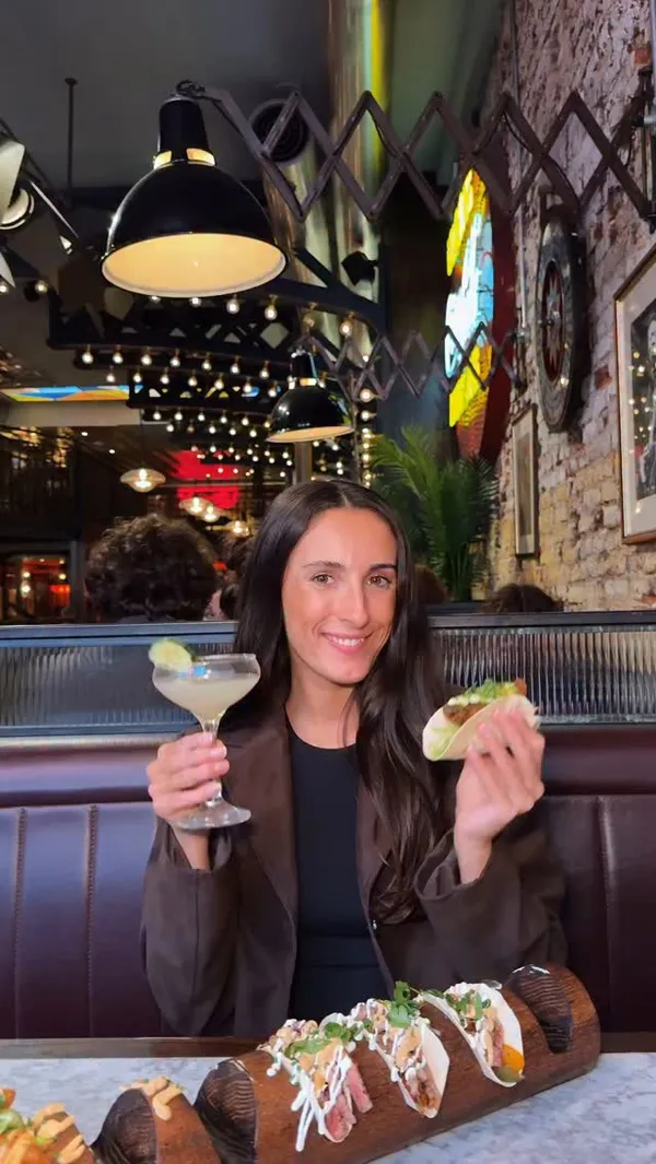 The video features a woman at Maxwell's Bar & Grill in Covent Garden, London, promoting their "Taco Social Club" offer. It showcases various tacos presented on a wooden board, including close-ups of different fillings and toppings. Several cocktails, including margaritas, are also featured with close-ups and garnishes like cucumber, lime, and pineapple. The video includes shots of the restaurant's interior, highlighting its ambiance and neon signs. The main focus is on the food and drink offer.