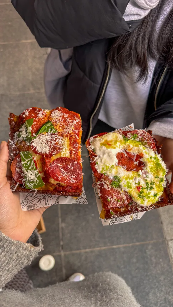 The video showcases three food spots in Ealing, West London. It starts with the influencer walking towards a restaurant, followed by shots of the exterior of Ealing Broadway. The first restaurant featured is Sarv's Slice, showing Detroit-style pizza slices with various toppings, including pepperoni and a creamy white topping, accompanied by a dipping sauce. The influencer is then seen taking a bite of the pizza. The second restaurant is Three Uncles, presenting dishes like sesame prawn toast, noodles with roasted duck and chicken, and green vegetables. Chopsticks are used to pick up noodles and prawn toast. The third restaurant is Butchies, featuring a chicken burger with cheese sauce, fries, fried chicken pieces dipped in cheese sauce, and macaroni and cheese. The video ends with a shot of the restaurant's exterior.