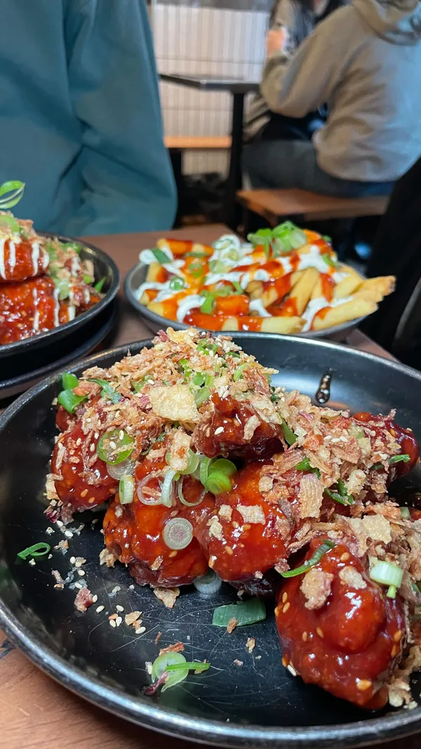 The video showcases a meal at Wingman Chicken, a restaurant specializing in chicken wings and sides.  It features various dishes, including several types of chicken wings with different toppings (e.g., fried onions, sesame seeds), truffle mac and cheese with beef brisket, and fries with sauces. The food is presented on plates and in small serving dishes. The setting is a casual, dimly lit restaurant.  The main focus is on the food itself, highlighting its appearance and variety.