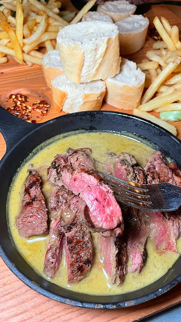 The video showcases a meal from Swiss Butter, a London restaurant. The setting is the restaurant itself. The food shown is a beef filet in a green sauce, accompanied by bread, fries, and salad. The presentation is appealing, emphasizing the generous portion sizes and visually pleasing arrangement of food items. Dietary information is not explicitly provided. The main focus is on the meal showcase, emphasizing the quality and taste of the food.