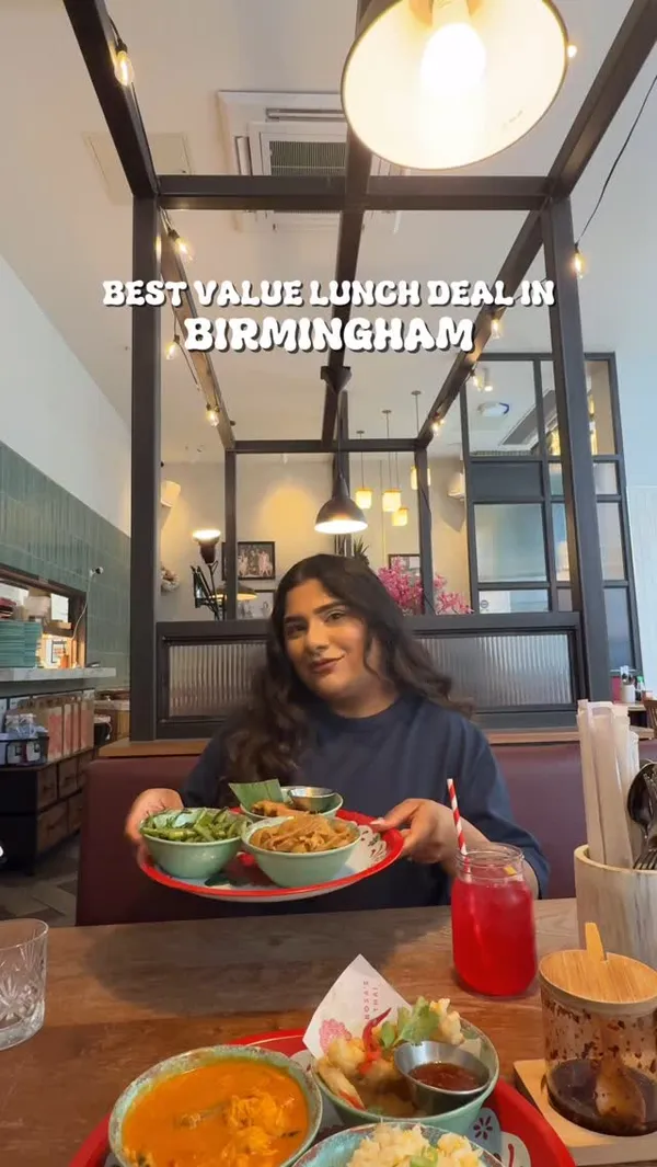 The video features an influencer at Rosa's Thai restaurant in Birmingham, showcasing their new Saiphin's set lunch menu. The menu offers three dishes for £14. The video shows the restaurant interior, the menu, a tangy Thai soda, and various Thai dishes including spring rolls, morning glory, Pad See Ewe, Thai calamari, egg fried rice, and a curry, presented on traditional Thai trays. The influencer is shown tasting the food and expressing positive reactions.