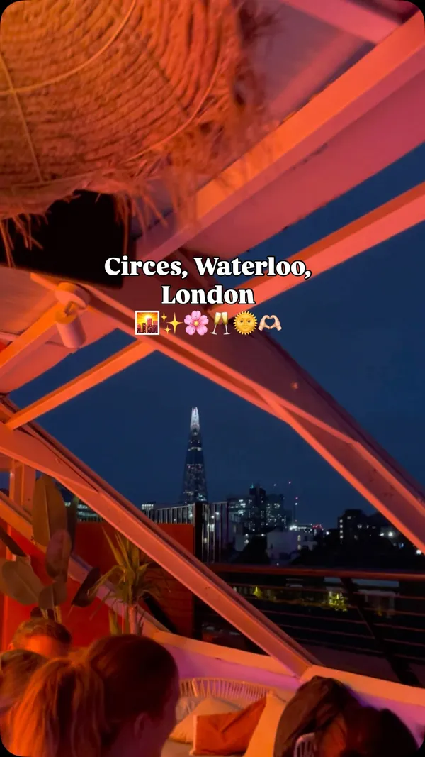 The video provides a tour of Circe's, a rooftop bar in Waterloo, London. It begins by showing the entrance and menu, then transitions to panoramic views of the London skyline, including the London Eye and The Shard. The video features a group of friends enjoying various cocktails, such as a Lychee Bramble, and sharing plates of food including calamari with aioli, prawns, seasoned fries, and what appears to be chicken. The atmosphere transitions from day to a vibrant evening setting with pink lighting. The video concludes with a toast with champagne, emphasizing the social and celebratory vibe of the venue.
