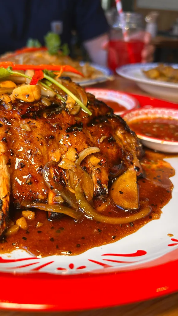 The video features an influencer visiting Rosa's Thai restaurant in Manchester. It showcases several dishes and drinks, including the new Thai-Spiced Pork Ribs served with rice and dips, Chicken Pad Thai, Chicken Satay with peanut sauce, a Seabass and Mango Salad, and two drinks (Nam Dang Munau soft drink and another cocktail). The influencer highlights the tenderness of the pork ribs and expresses enjoyment of the food and drinks. The restaurant interior is also briefly shown.