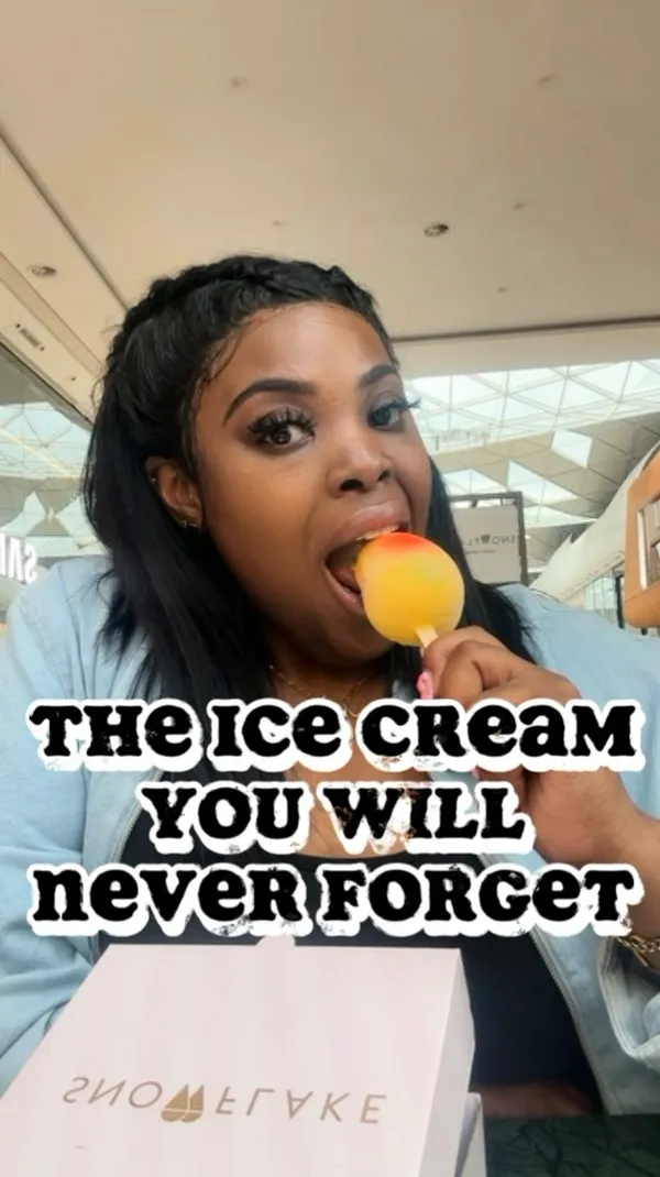 A woman unboxes and tries two desserts from Snowflake Gelato in Westfield White City. The main feature is the 'Snow Mango,' a mango-shaped mango sorbet with a white chocolate and lemon shell. She also tries a pistachio cannoli ice cream bar. The video includes shots of the shop's dessert display and the creator's enthusiastic reactions while eating.