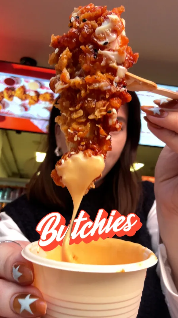 A food review video of Butchies, a fried chicken restaurant in Shoreditch, London. The video showcases several menu items, with a primary focus on the limited edition Kimchi Honey Butter Tenders. Other items featured include a Buffalo Burger, mac and cheese, fries, a melted Red Leicester cheese sauce, and OG gravy. The creator is shown trying each item and providing her opinion.