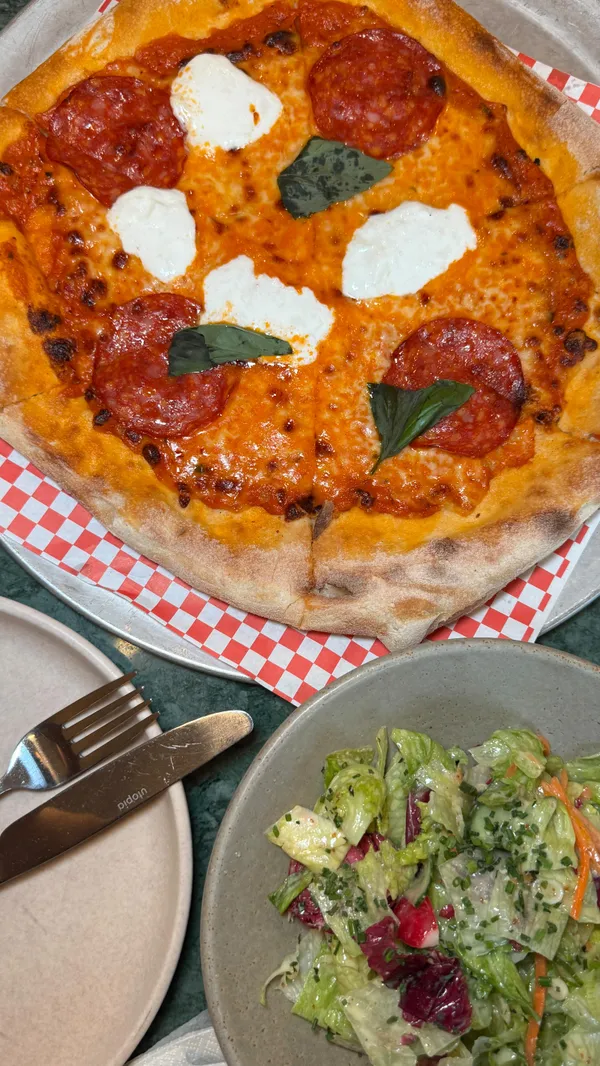 The video showcases a visit to Eve Kensington. It features close-ups of a pepperoni pizza with mozzarella and basil, a mixed green salad with shredded carrots and radicchio, and an Aperol spritz. It also shows the restaurant's interior, including the reception/lounge area, dining space, bar area with various bottles, and a bartender preparing drinks. A menu is also briefly shown.