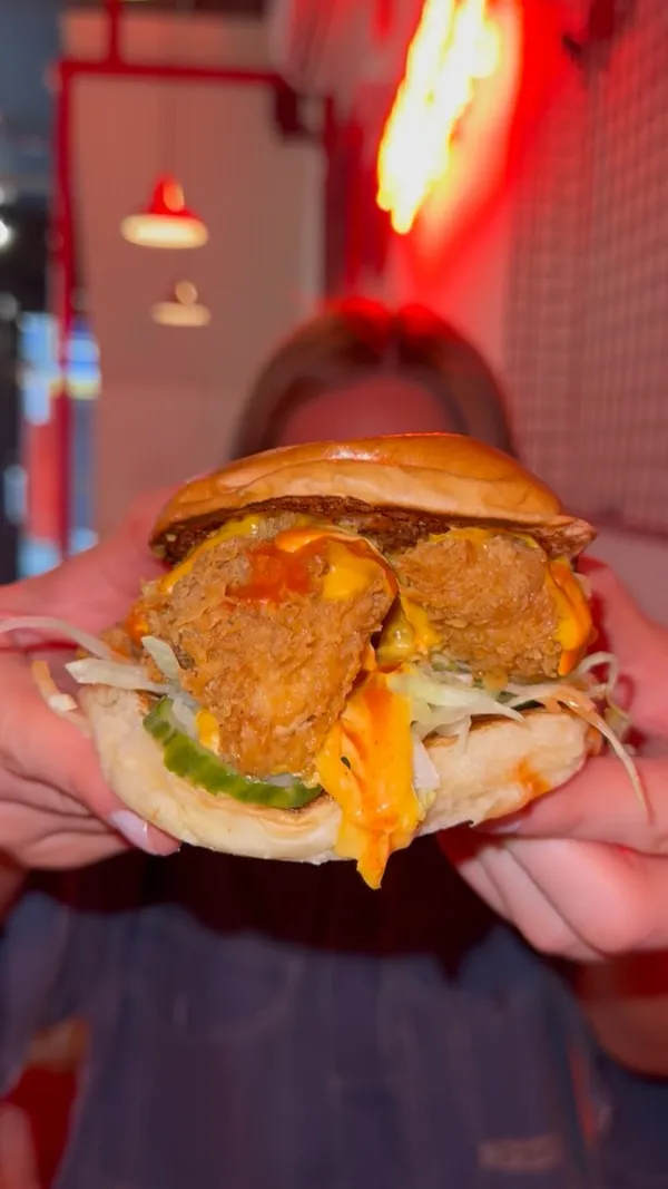 The video showcases a review of Butchies London, a restaurant specializing in buttermilk fried chicken. The video begins with the influencer on a Lime bike, expressing excitement about reviewing Butchies. The video then transitions to the restaurant's sign and showcases a chicken burger with cheese, lettuce, and sauce. The influencer takes bites of the burger and comments on its softness. The video also features chicken strips with various dipping sauces, including cheese and BBQ. A male hand pours chili honey over the chicken strips, and a man is shown eating them. The video concludes with the influencer eating fries with sauce and taking more bites of the chicken burger.