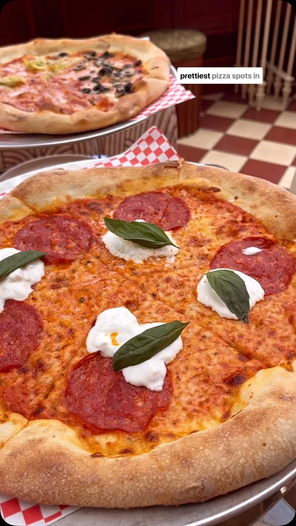 This video showcases the Eve restaurant located in the Ember Locke Hotel in Kensington, London. The video features the restaurant's interior, exterior, and food offerings. The food shown includes two pizzas: a New York pizza with salami, straciatella, and basil, and a Four Seasons pizza with ham, mozzarella, artichokes, and olives. Also featured are buffalo chicken wings with blue cheese dip and aperol spritzes. The presentation of the food is highlighted, with close-ups of the pizzas and wings. The main focus is on showcasing the restaurant's ambiance and food quality.