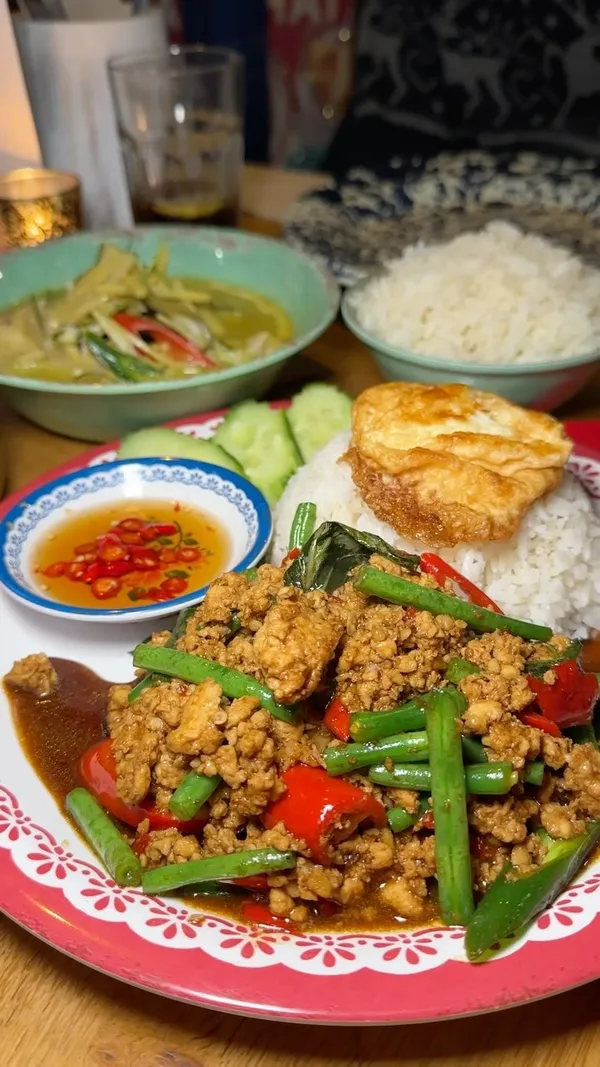 The video showcases a variety of Thai dishes from Rosa's Thai restaurant, highlighting their Thai Feast Menu. The setting is a restaurant environment. The food items include a Classic Platter with spring rolls and chicken, Prawn Doughnuts, Chicken Green Curry, Chilli & Basil Stir Fry with Minced Chicken, Somtum Brownie with ice cream, and Mango & Sticky Rice. The presentation emphasizes the vibrant colors and textures of the dishes. The video also shows a drink, possibly Thai iced coffee. The main focus is on showcasing the variety and flavors of the Thai Feast Menu.