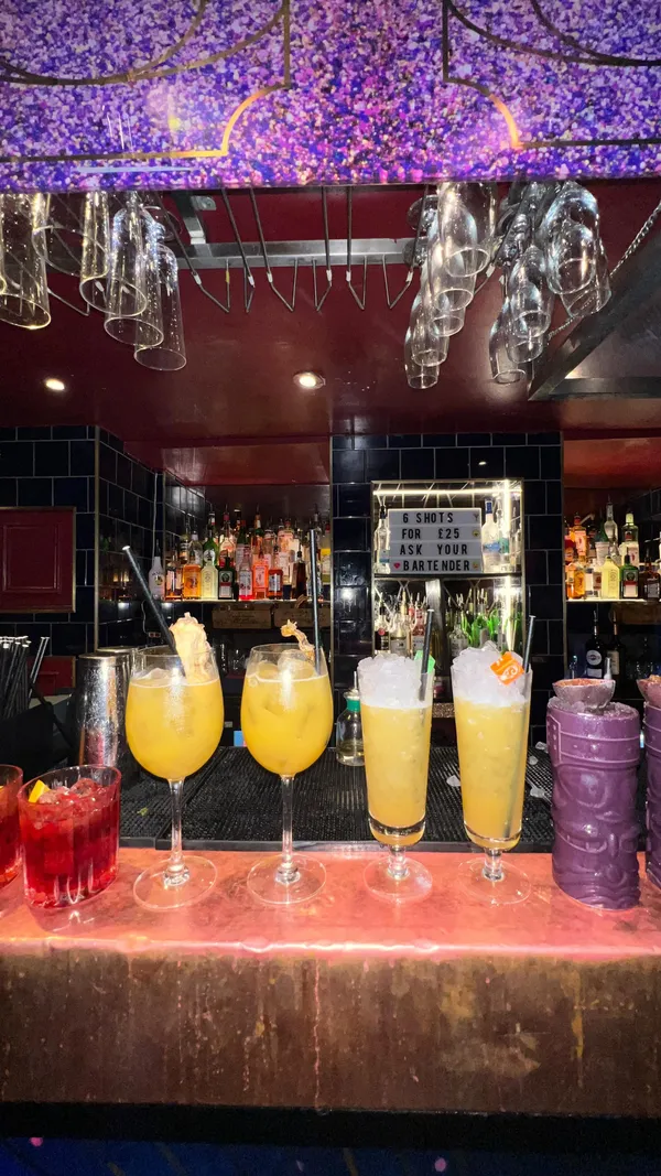 The video showcases Escapologist Bar, a quirky basement bar in Covent Garden, London. It highlights the bar's ambiance, featuring red lighting, unique artwork, and a checkerboard floor.  The video focuses on cocktail preparation and presentation, showcasing several colorful cocktails such as the 'Starburst Boogie' and 'Coco Loco.' The cocktails are garnished with fruits and presented in various glasses. Happy hour deals (2-4-£12) are mentioned.  The video includes shots of people enjoying the cocktails in a dimly lit, intimate setting.  No dietary information is provided.