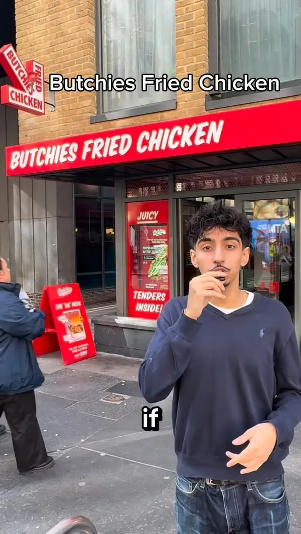 A food review video of 'Butchies Fried Chicken'. The creator introduces the restaurant from the outside, shows the menu, and then proceeds to try two different chicken burgers and a side of Kimchi Honey Butter Tenders. The burgers shown are large and filled with ingredients like coleslaw, bacon, and cheese with buffalo sauce. The creator eats the food on camera, expressing his enjoyment and describing the taste and texture.