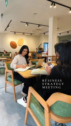 Two professionals strategizing in a cute café, enjoying matcha and bakery treats while planning business expansion in India.