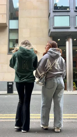 Two friends wearing stylish @blakely_women hoodies, smiling and enjoying each other's company in a vibrant setting.