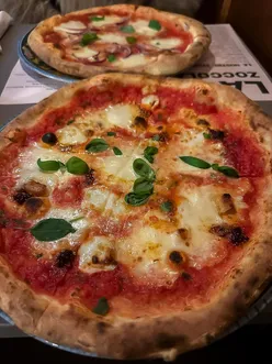 Customer enjoying nduja and veggie pizzas at Zoccola in Amsterdam, seeking more toppings on their meal.