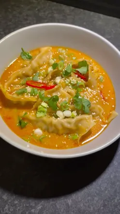 Steaming bowl of gyoza broth with pork gyozas, rice noodles, and fresh toppings for an easy dinner recipe.