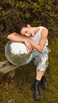 Two friends posing with a giant disco ball in a field, capturing playful moments on a vibrant, sunny day.