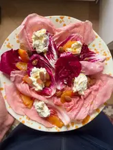 A vibrant, overhead shot of a winter salad featuring radicchio, blood orange segments, cottage cheese, and toasted almonds, presented on a speckled plate.