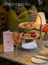 A high-angle shot of an afternoon tea stand featuring delicate pastries and a cocktail, set on a marble table in a restaurant setting.