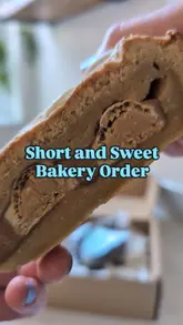 A short, handheld unboxing video showcasing an Easter-themed treat box from a vegan bakery. The video features close-up shots of various baked goods, including a cookie pie, brownies, and blondies, with the creator breaking them open to reveal their textures.