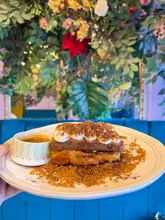 A close-up, handheld shot of a dessert dish, likely Tiramisu French toast, presented against a floral wall background. The image captures the subject clearly but lacks professional food styling.