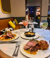 A high-quality, well-composed shot of a Sunday roast dinner at a restaurant, featuring roast beef, Yorkshire puddings, and cocktails.