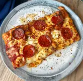 A top-down, close-up shot of a single slice of pepperoni pizza drizzled with hot honey, served on a grey plate.