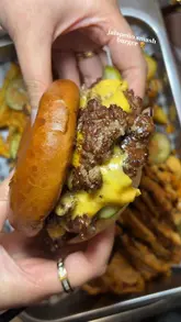 Close-up of a smashburger from Dark Burg, featuring two patties, melted cheese, and fresh toppings, next to loaded fries.