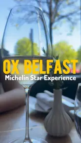 A montage of a lunch service at OX Belfast, featuring close-up shots of various courses, including bread, seafood, meat, and petit fours. The video focuses on the presentation of the food with minimal context of the venue itself.