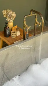 A cinematic montage showcasing a cabin staycation located an hour from London. The video highlights the cozy interior, the scenic countryside surroundings, outdoor amenities like a wooden tub and fire pit, and relaxing moments including breakfast and evening drinks.