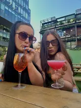 A photo of two women posing with cocktails at an outdoor venue, capturing a social, sunny atmosphere.