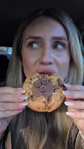 A creator reviews a box of cookies and brownies from 'My Dessert Plug' while sitting in a car, highlighting the texture and flavors of the treats.