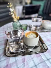 A high-quality, well-composed shot of a specialty coffee served on a metal tray, featuring clear latte art and a glass of water. The shallow depth of field draws focus to the coffee, while the soft, natural lighting creates an inviting atmosphere.