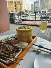 A table setting featuring aromatic duck, dim sum, and a drink, overlooking a marina at Banquet 88.