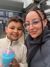A casual selfie of a mother and son holding a bright blue and pink slushie drink outside a venue entrance, likely taken during a family day out.