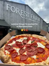 A casual, first-person perspective shot of a pepperoni pizza in a takeaway box, held up in front of the Forest Farm building. The image serves as an introduction to a list of summer recommendations in the Aberdeen area.