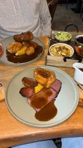 A montage video showcasing a Sunday lunch experience at The Ticket Office in Ilkley, featuring shots of the venue's interior, live music, and various courses including bread and dips, a Sunday roast, and a cheese board.
