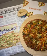 A top-down shot of a cooked frozen pizza on a wooden board, placed on top of a newspaper article about the product's return to shelves.