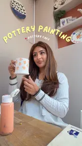 The video features a creator visiting a pottery cafe, showing the selection of unpainted ceramics on shelves, the painting process with various colors, and the finished mug. It highlights the activity as a social, therapeutic experience to do with friends.
