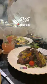 A couple visits Ava in Romford, showcasing the restaurant's interior, cocktails, and a variety of dishes including red velvet tempura prawns, chicken tacos, lamb cutlets, black onyx ribeye, lamb shank, and grilled branzino.