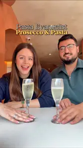A couple reviews their dining experience at Pasta Evangelists, highlighting the 'build your own pasta' concept. They showcase various dishes including garlic and chilli king prawns, aubergine parmigiana, chicken and mushroom tagliatelle, truffle cacio e pepe, and desserts like tiramisu and strawberry cheesecake, all paired with prosecco.