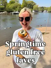 A casual, outdoor shot of a person holding a gluten-free bun by a river, likely taken at a market or outdoor venue.