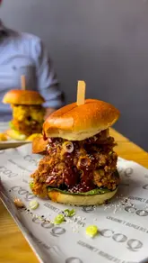 A promotional reel featuring a visit to 'Coq' in Bristol, showcasing their gourmet burger menu, loaded tater tots, cocktails, and dessert. The creator provides a positive review of the food quality and atmosphere.