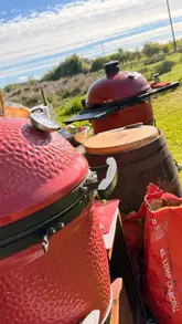 A montage video documenting a BBQ event at Auldton Stoves, featuring various meats being cooked on Kamado Joe grills, scenic driving shots, and social interaction.