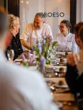 A high-quality, professional photograph capturing a warm, candid moment between chefs and guests at a restaurant table. The image conveys a sense of hospitality and exclusivity, with a shallow depth of field that draws attention to the subjects while maintaining a polished, inviting atmosphere.