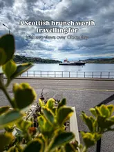 An atmospheric, scenic shot taken from inside a venue looking out over Oban Bay, featuring a ferry in the distance and framed by foreground foliage.