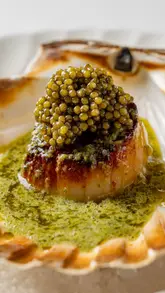 A short, polished video showcasing the preparation of a roasted hand-dived XL scallop dish, topped with caviar and Cafe de Paris butter, by a private chef.